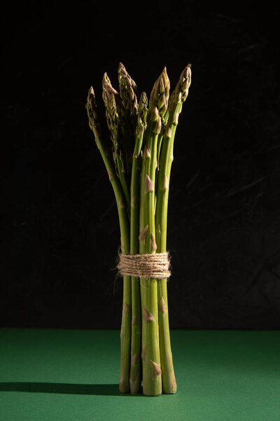 Fresh stalks of green asparagus on a dark green background. Vegan, healthy eating, diet concept. Organic vegetables. Gloomy mood, low key photo.