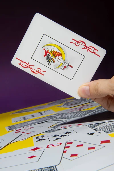 Joker card in hands on a yellow and purple background with cards.