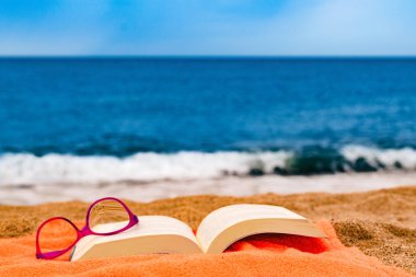 book and glasses on the beach towel with the sea in the background