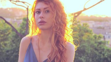 Şehirdeki güzel kızıl saçlı kadın sorgulayarak kameraya bakıyor.