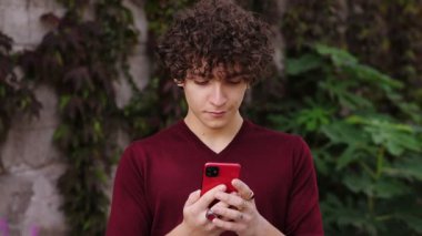 Genç adam akıllı telefonuyla yazarken ve sosyal medyada yazı okurken gülümsüyor.