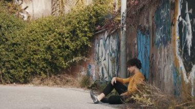 Depresyonda olan genç bir adam sokakta duvara yaslanıyor ve kafasını eğiyor.