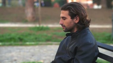 Parktaki bankta oturan düşünceli yakışıklı genç adam gökyüzüne dua ederek bakıyor.