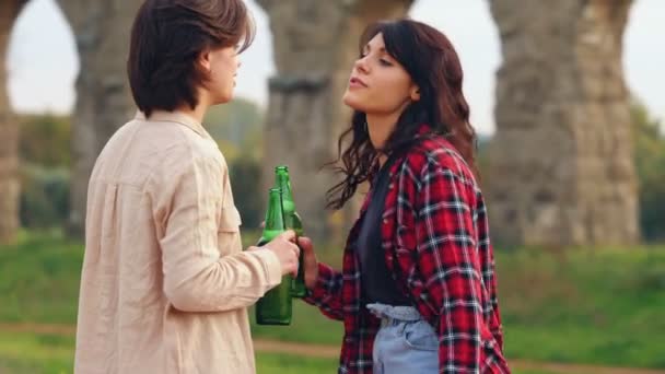 ビールを飲みながら公園でおしゃべりしたり踊ったりする2人の美しい若い友達のスローモーション — ストック動画