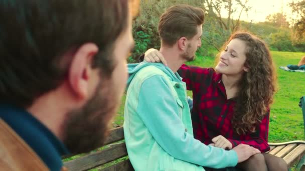 Fiatal Megcsókolja Barátját Egy Padon Parkban Nézi Érdeklődéssel Egy Srác — Stock videók