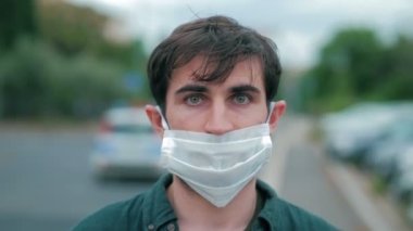 Sokaktaki genç adamın portresi. Burnunun altındaki maskeyi takıyor. Kameraya ciddi ciddi bakıyor.