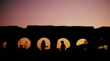 Roma 'daki bir su kemerinin kemerleri arasında gün batımında dans eden iki genç kadının güzel manzarası.