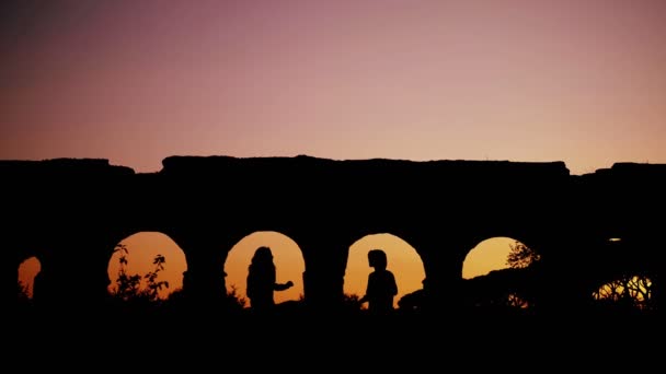 两个年轻女子在夕阳西下的阳光下在罗马一条渡槽拱门之间跳舞的美丽景象 — 图库视频影像
