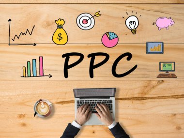Tahta masanın üzerinde dijital pazarlama simgeleri olan PPC metni. Dizüstü bilgisayarda arama yapan bir iş adamı, tıklama başına öde. Dijital çevrimiçi pazarlama ve İnternet teknolojisi kavramı.