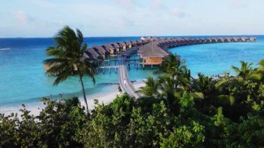 Maldives. Aerial 4k shot of Young man in white clothes walks on wooden bridge to luxury water bungalows. Maldives island resort.