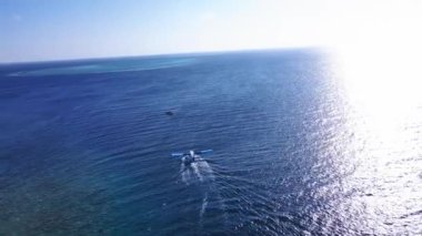 Seaplane takes off in the Indian Ocean with Tropical Maldivian atoll island in the background. Coral reef and turquoise sea water. Scenic seascape. Vakkaru, Maldives. High quality 4k footage