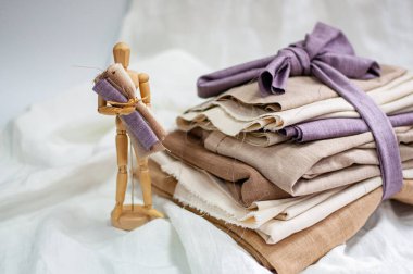 Cotton fabric stacked in layers with a wooden figurine of a little man. Natural fabric