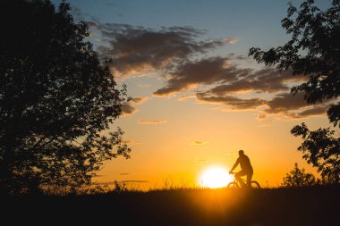 Bir bisikletçi, gün batımının güzel bir konturunun arka planına karşı bir tarlada yol alır. Güzel gün batımı. Doğanın fotoğrafı. Hız teması.