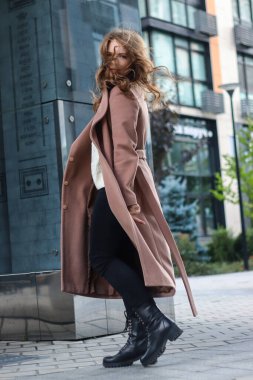 Sarışın, uzun saçlı, bej ceketli bir kızın sokak fotoğrafı. Büyük şehirde fotoğraf çekimi..