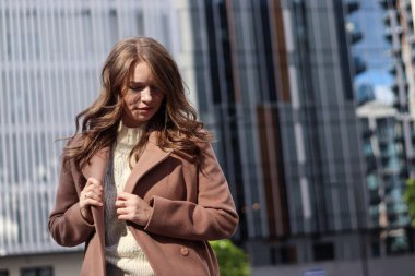 Sarışın, uzun saçlı, bej ceketli bir kızın sokak fotoğrafı. Büyük şehirde fotoğraf çekimi..