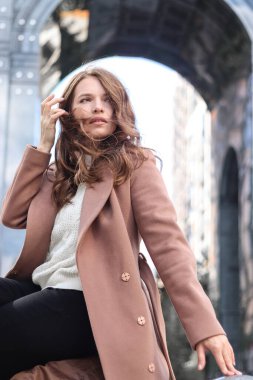 Sarışın, uzun saçlı, bej ceketli bir kızın sokak fotoğrafı. Büyük şehirde fotoğraf çekimi..