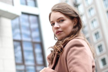 Sarışın, uzun saçlı, bej ceketli bir kızın sokak fotoğrafı. Büyük şehirde fotoğraf çekimi..