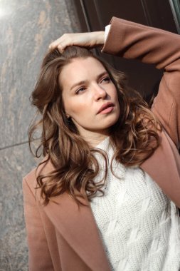 Sarışın, uzun saçlı, bej ceketli bir kızın sokak fotoğrafı. Büyük şehirde fotoğraf çekimi..