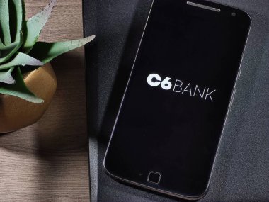 Akıllı telefon ekranındaki C6 Bank logosu ahşap masadaki defterin üstünde. C6 Bank Brezilya 'nın dijital bankasıdır..