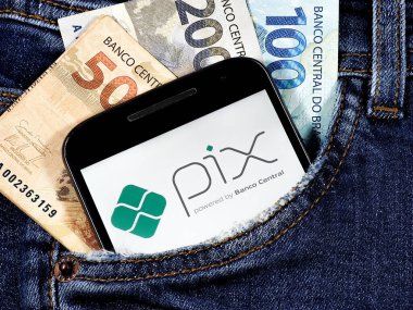 Ekranda Pix logosu olan akıllı telefon cebinde 100 reais 200 reais ve 50 reais ile birlikte. Pix, Brezilya 'nın ani ödemesi.