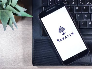 J. Safra Sarasin Ltd Bankası, ahşap masanın üstündeki defterin üstündeki akıllı telefon ekranında. Safra Sarasin Ltd İsviçre 'de bulunan özel bir bankadır..