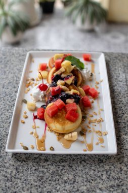 Üstü tahıllı ev yapımı krep, bal, karpuz dilimi, ananas, böğürtlen ve beyaz tabakta krema ve estetik desenli arka plan..