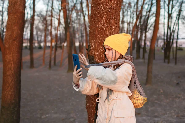 Dziewczyna z eko-siatki torba z owocami używa telefonu komórkowego w jesiennym parku, zero odpadów i zrównoważonego stylu życia — Zdjęcie stockowe