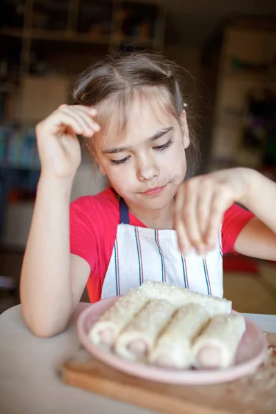 Chica cocinando salchicha enrollada en phyllo pastelería para el desayuno, poco chef disfruta de sabrosa merienda — Foto de Stock