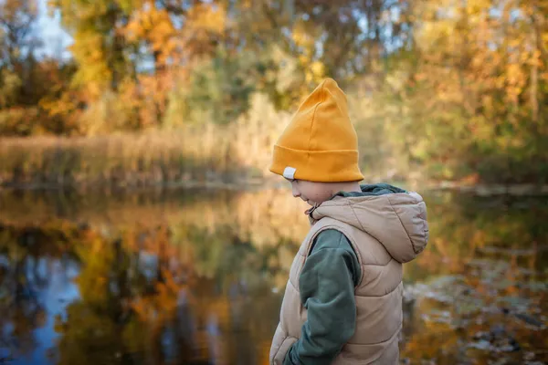 Niño mira hermosa vista del bosque de otoño y su reflejo en el agua del lago, en lo profundo de los pensamientos — Foto de Stock