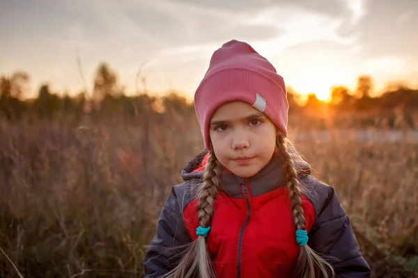Portrait of pensive preteen girl standing among a dry meadow over beautiful autumn sunset — Stock Photo, Image