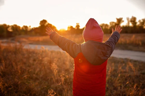 Lány áll a kezét nyitott és felemelt, hogy megfeleljen a naplemente, és hálát ad neki között száraz rét — Stock Fotó