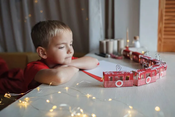 Menino sonhos perto de calendário de advento trabalhada como estância de esqui ou trem com rolos de papel higiênico em casa — Fotografia de Stock