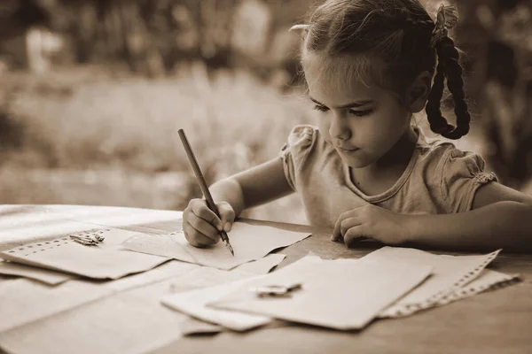 Ретро и винтажная концепция. Маленькая девочка пишет письмо чернильной ручкой, старые конверты — стоковое фото