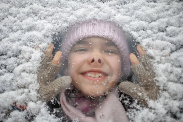 Zabawny portret dziewczyny w ciepłej czapce przez śnieżne szyby samochodowe podczas zimowej wycieczki rodzinnej — Zdjęcie stockowe