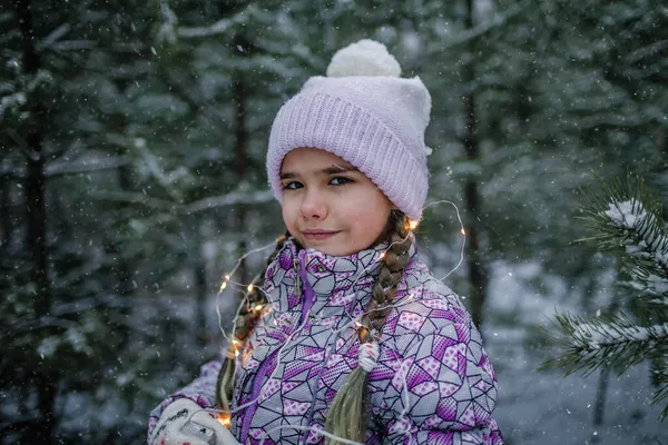 Flicka, ler och skrattar, leker med glödande krans under promenader i skogen på snön dag — Stockfoto