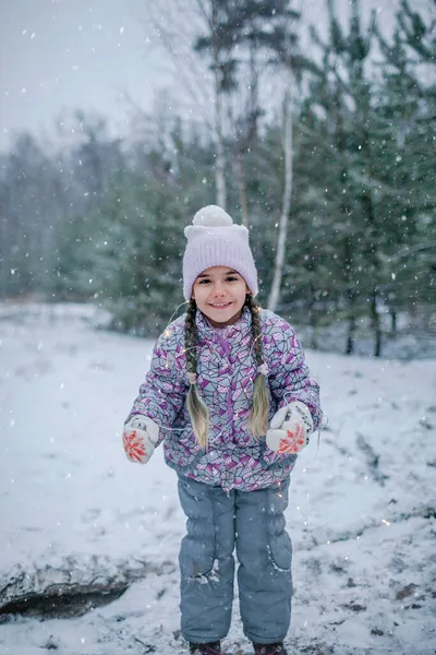 Girl, smiling and laughing, plays with glowing garland during walking in forest on snowing day — Stock Photo, Image
