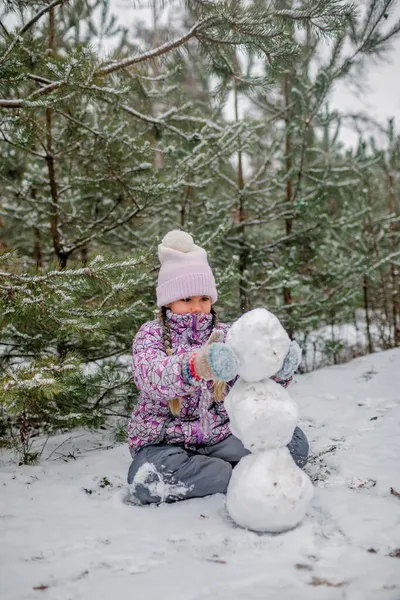 Chica hace un muñeco de nieve de la primera nieve durante la familia caminando en el bosque en el día de niebla — Foto de Stock