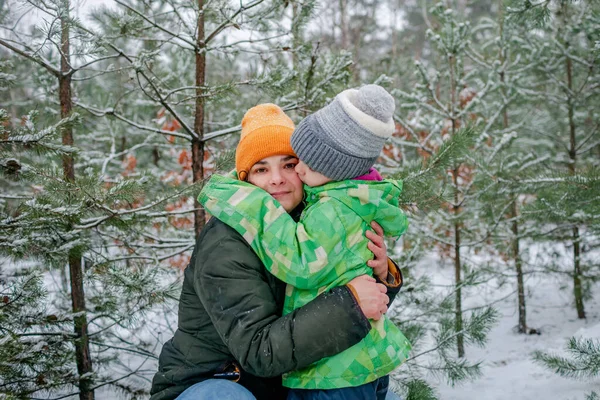 Chłopiec całuje mamę ze szczęściem, że spadł pierwszy długo oczekiwany śnieg, rodzina spaceruje po lesie — Zdjęcie stockowe