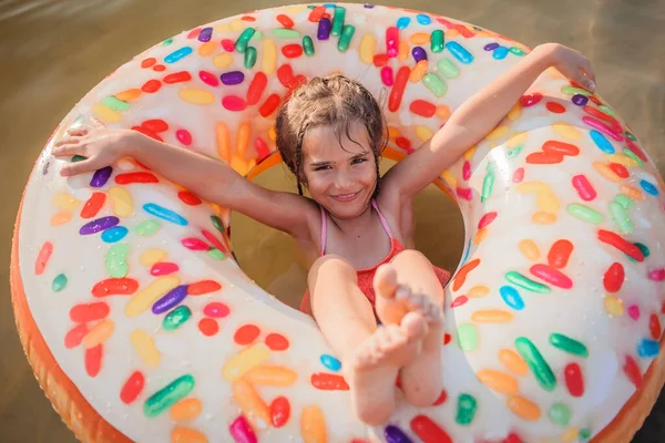 Ragazza si diverte su grande anello gonfiabile ciambella sul lago nella calda giornata estiva, felice estate, campagna — Foto Stock