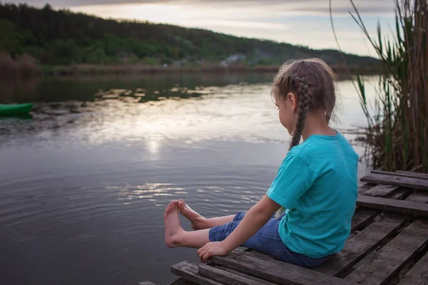 Chica se sienta en el puente de pontón en el lago y disfruta de una cálida noche soleada, feliz verano, campo — Foto de Stock