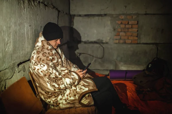 Украинский юноша сидит в бомбоубежище и читает последние новости о российских захватчиках — стоковое фото