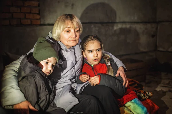 Grandmother hugs little Ukrainian kids, they sit out attack of Russian aggressor in bomb shelter — Stock Photo, Image