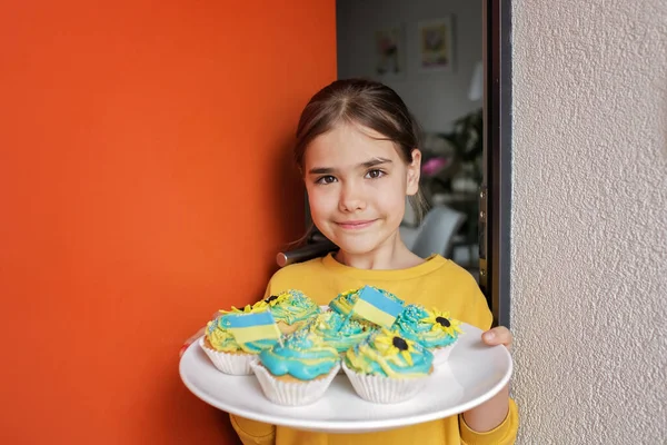 乌克兰女孩，邻居们给她端来带有黄色和蓝色奶油的纸杯蛋糕当早午餐 — 图库照片