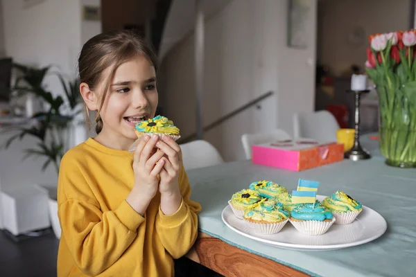 Ukrán lány, akinek a szomszédok hozott cupcakes krémmel sárga és kék színű villásreggeli — Stock Fotó