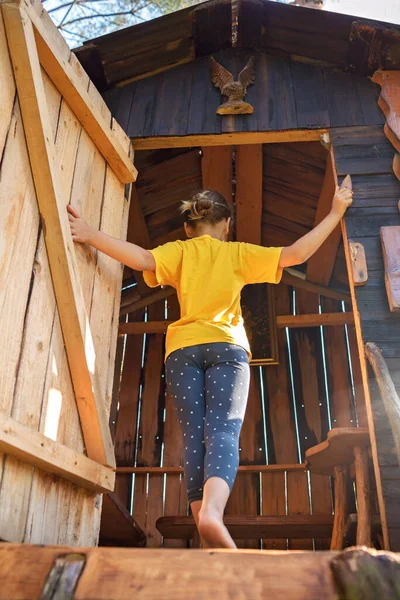 Kız, arka bahçedeki el yapımı ağaç evde oynuyor. Yaz etkinliği, mutlu çocukluk, kır evi.
