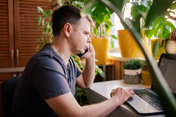 Man works with laptop remotely from home. Distant work place with green-nature inspired home office