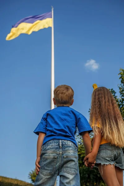 穿黄色衣服的女孩和穿蓝色衣服的男孩看着乌克兰最大的国旗。为和平与胜利祈祷 — 图库照片