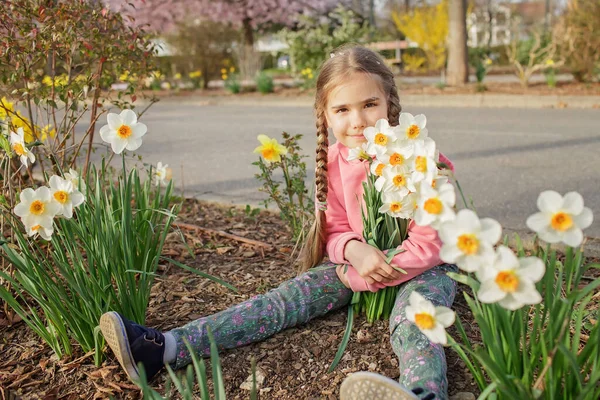 Rózsaszín kapucnis lány virágzó nárcisz illatot érez, miközben a tavaszi kertben sétál. — Stock Fotó