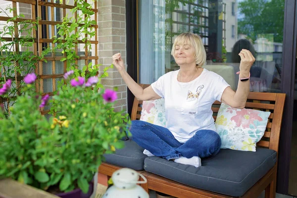 Mulher sênior relaxa em ioga posar na varanda em casa. aposentadoria ativa, esporte, bem-estar em qualquer idade — Fotografia de Stock