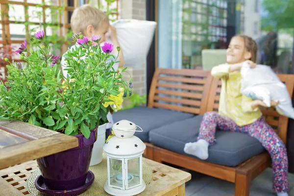 A gyerekek párnacsatáznak otthon az erkélyen. Zöld növények. Terasz élet vakáción. Koncentrálj a virágra. — Stock Fotó